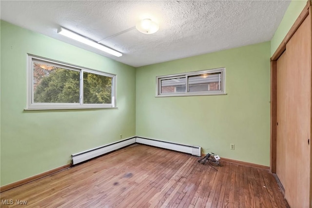 empty room with a baseboard heating unit, baseboards, a textured ceiling, and hardwood / wood-style flooring