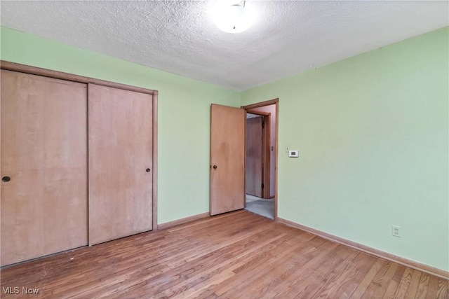 unfurnished bedroom featuring a closet, baseboards, a textured ceiling, and wood finished floors