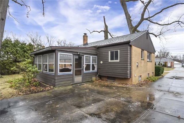 back of property featuring a sunroom, brick siding, a chimney, and a patio area