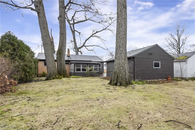 back of property featuring brick siding, a chimney, and a sunroom