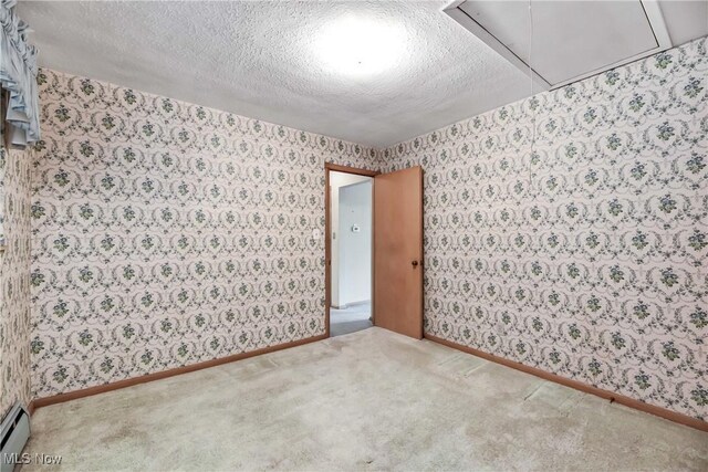 unfurnished room with a textured ceiling, attic access, and wallpapered walls