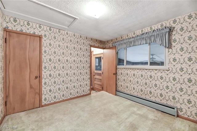 unfurnished room featuring carpet, a baseboard radiator, wallpapered walls, attic access, and a textured ceiling