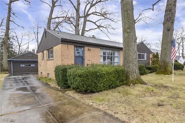 view of front of property featuring an outbuilding, a garage, brick siding, and roof with shingles