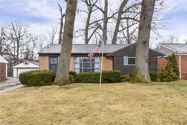 view of front facade with an outbuilding, a front yard, a shingled roof, a garage, and brick siding