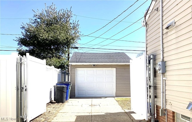 detached garage featuring concrete driveway and fence