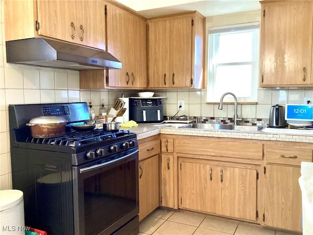 kitchen featuring light tile patterned floors, stainless steel range with gas stovetop, a sink, under cabinet range hood, and backsplash