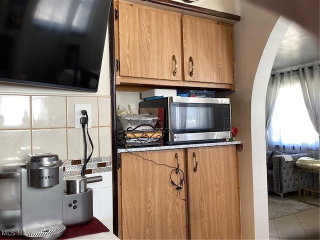 kitchen with stainless steel microwave, brown cabinetry, tasteful backsplash, and tile patterned floors