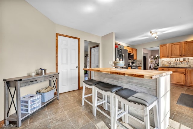 kitchen with butcher block counters, a kitchen breakfast bar, backsplash, and stainless steel appliances