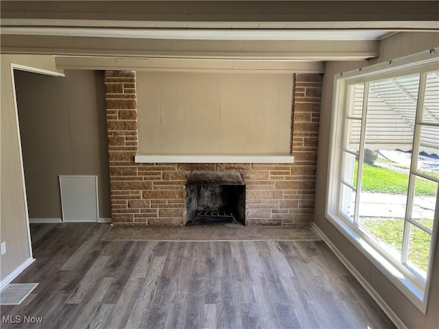 unfurnished living room with a stone fireplace, wood finished floors, visible vents, and baseboards