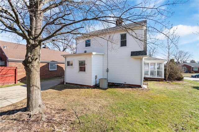 rear view of house featuring fence, a yard, a sunroom, a chimney, and central air condition unit