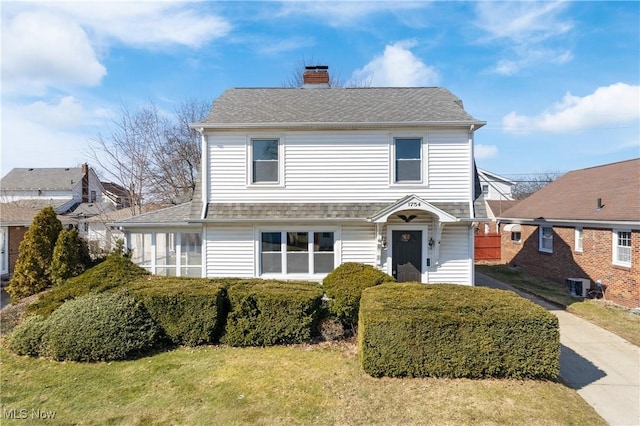 view of front facade with central air condition unit, a chimney, a front lawn, and a shingled roof