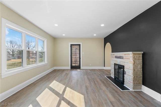 unfurnished living room featuring baseboards, a stone fireplace, and wood finished floors