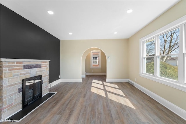 unfurnished living room with baseboards, a stone fireplace, recessed lighting, wood finished floors, and arched walkways