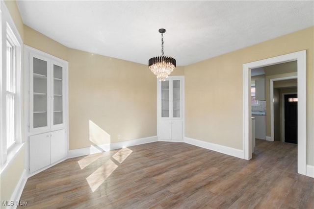 unfurnished dining area featuring a chandelier, baseboards, and wood finished floors