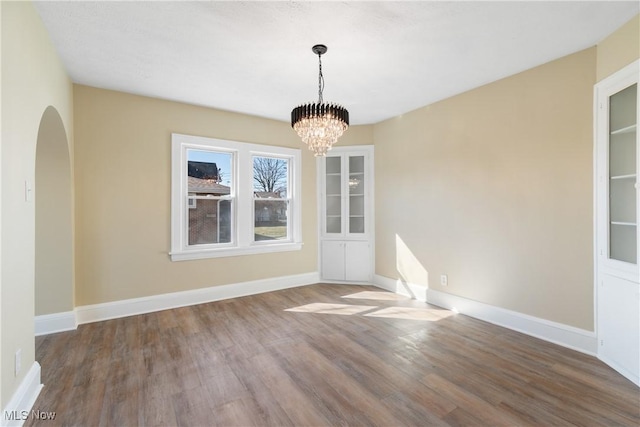 unfurnished dining area with arched walkways, a notable chandelier, baseboards, and wood finished floors