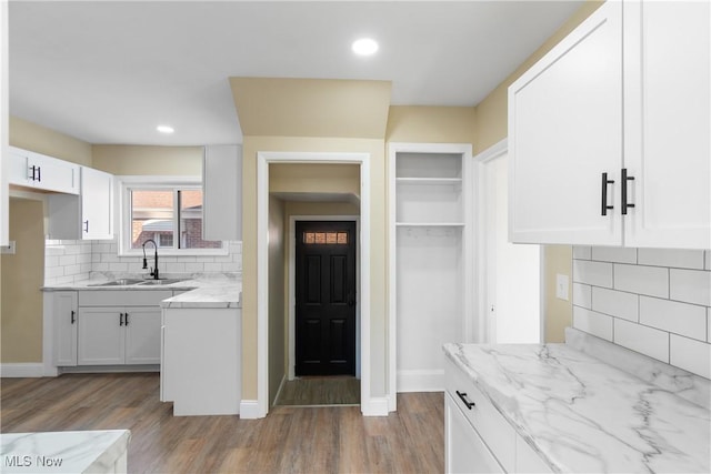 kitchen featuring light stone countertops, decorative backsplash, wood finished floors, white cabinets, and a sink