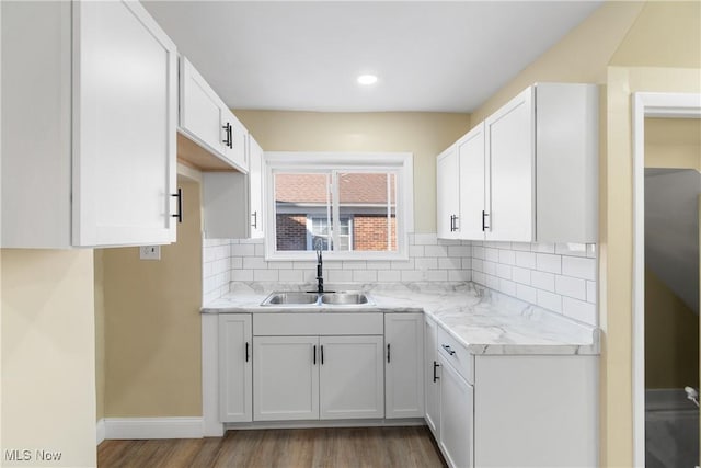 kitchen featuring light wood-style flooring, a sink, tasteful backsplash, white cabinets, and baseboards