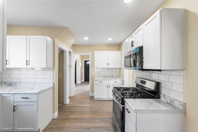 kitchen featuring light wood-style flooring, tasteful backsplash, white cabinetry, appliances with stainless steel finishes, and baseboards