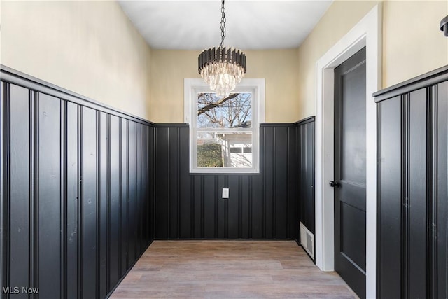 unfurnished room with a notable chandelier, light wood-style floors, visible vents, and wainscoting