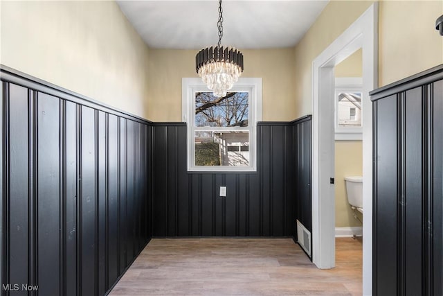 unfurnished room with a chandelier, a wainscoted wall, visible vents, and light wood-style floors