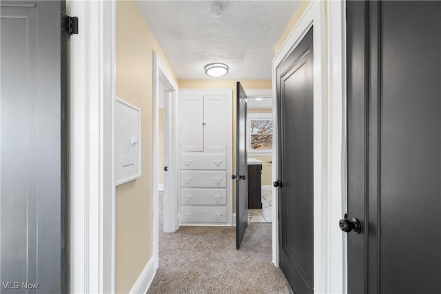 hallway with light carpet, a textured ceiling, and baseboards