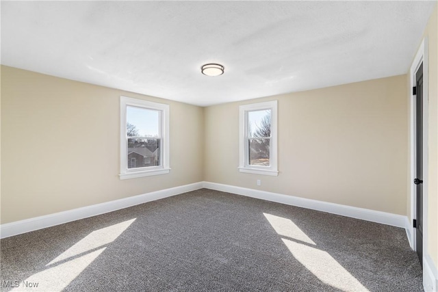 spare room with baseboards and dark colored carpet