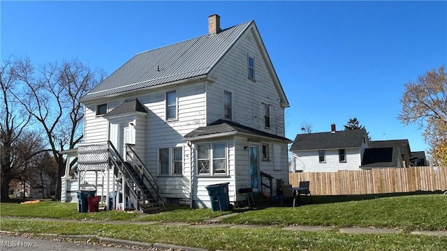 rear view of property featuring a standing seam roof, fence, a yard, metal roof, and a chimney