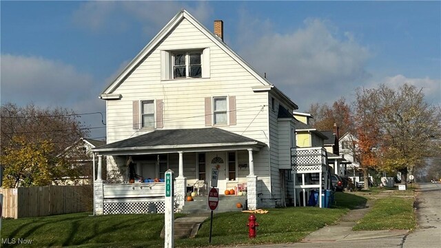 view of front of home featuring a porch, fence, and a front lawn