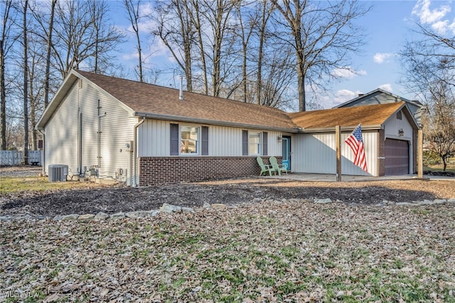 view of front facade featuring an attached garage, central AC unit, brick siding, and a shingled roof