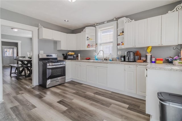 kitchen with gas stove, open shelves, white cabinetry, and a sink