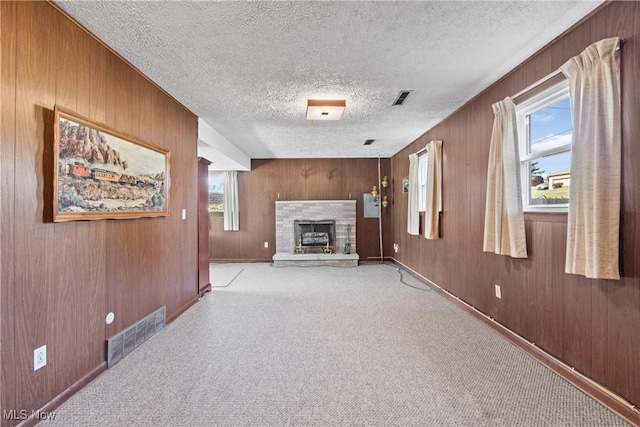 unfurnished living room with visible vents, light colored carpet, a healthy amount of sunlight, and a fireplace with raised hearth