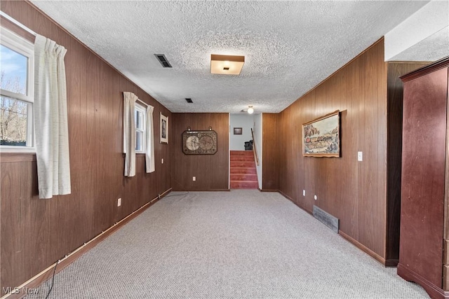 carpeted spare room with visible vents, a textured ceiling, wood walls, and stairway