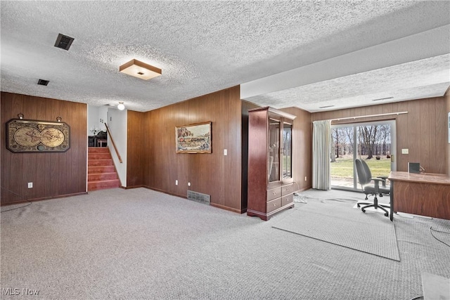 carpeted office space featuring visible vents, wood walls, and a textured ceiling