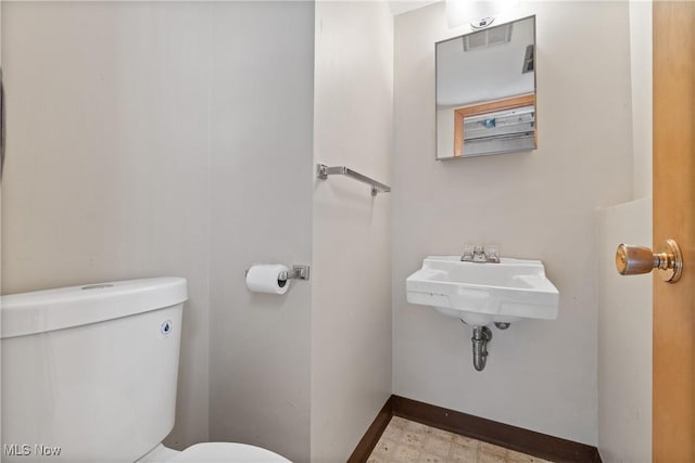 half bathroom featuring toilet, baseboards, and a sink