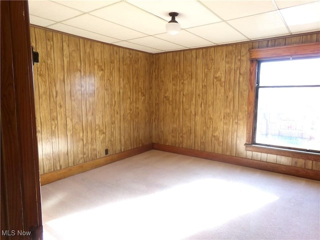 carpeted empty room featuring wooden walls, a paneled ceiling, and baseboards