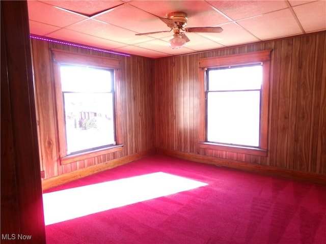 spare room featuring carpet floors, wooden walls, and a ceiling fan