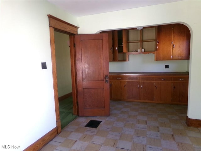 kitchen with visible vents, arched walkways, brown cabinetry, baseboards, and light floors