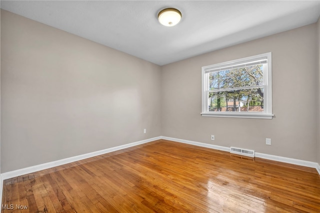 empty room with hardwood / wood-style floors, baseboards, and visible vents