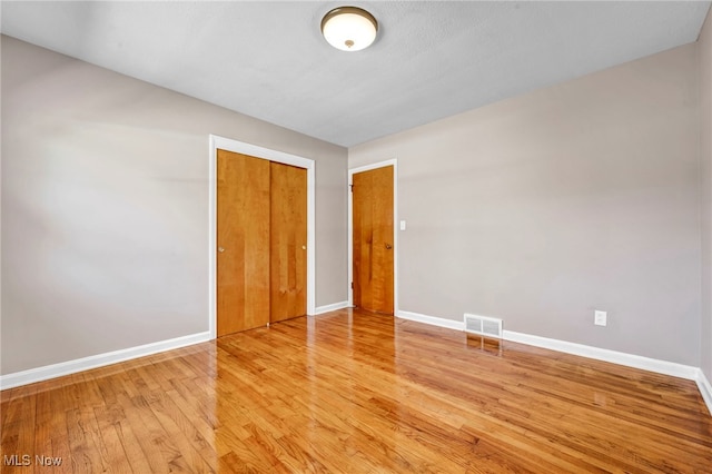 unfurnished bedroom with wood finished floors, visible vents, a closet, and baseboards