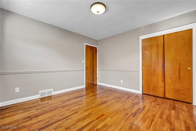 unfurnished bedroom featuring a closet, visible vents, baseboards, and wood finished floors