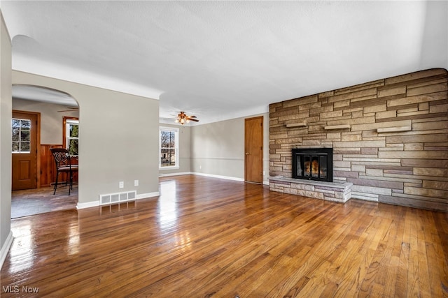 unfurnished living room with a wainscoted wall, visible vents, ceiling fan, a stone fireplace, and hardwood / wood-style flooring