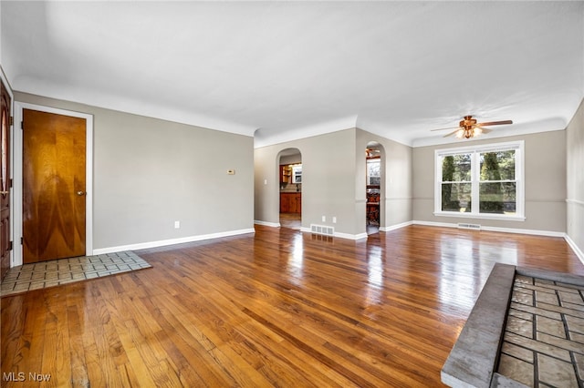 unfurnished living room featuring arched walkways, baseboards, and hardwood / wood-style flooring