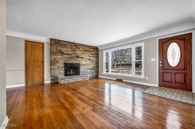 unfurnished living room with hardwood / wood-style floors, visible vents, a fireplace, and baseboards