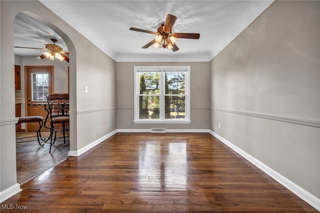 empty room with arched walkways, visible vents, baseboards, and wood finished floors