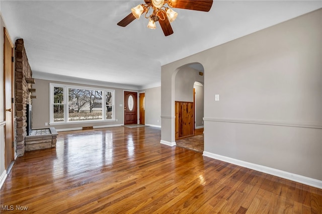 unfurnished living room featuring baseboards, arched walkways, a stone fireplace, and hardwood / wood-style flooring