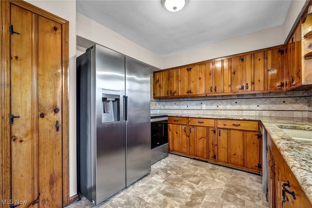 kitchen featuring tasteful backsplash, light stone counters, brown cabinets, stone finish floor, and stainless steel appliances