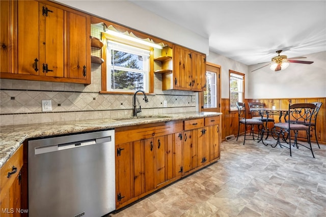 kitchen with a wainscoted wall, brown cabinets, a sink, open shelves, and stainless steel dishwasher