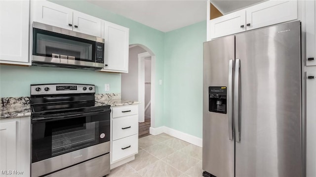 kitchen with light stone countertops, baseboards, arched walkways, appliances with stainless steel finishes, and white cabinetry