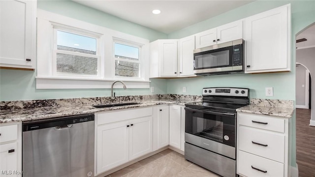 kitchen featuring a sink, white cabinetry, arched walkways, appliances with stainless steel finishes, and light stone countertops