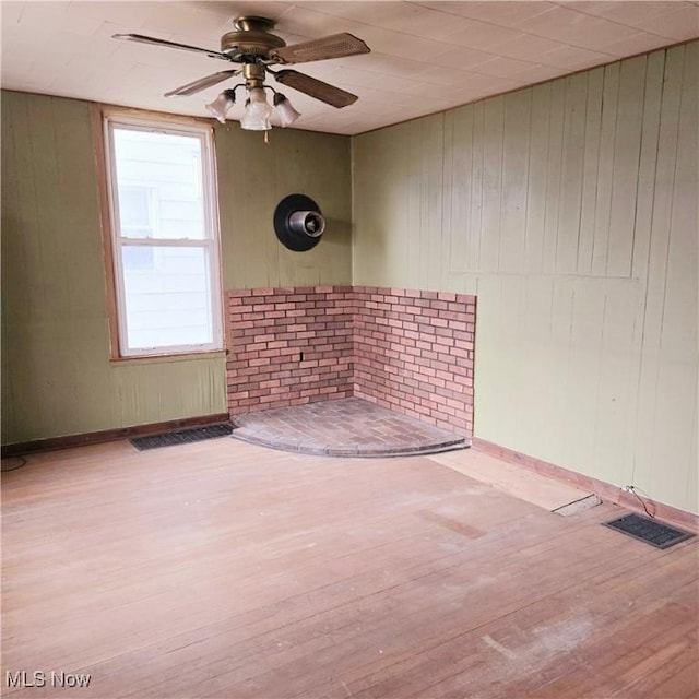 spare room featuring visible vents, wooden walls, wood finished floors, and a ceiling fan